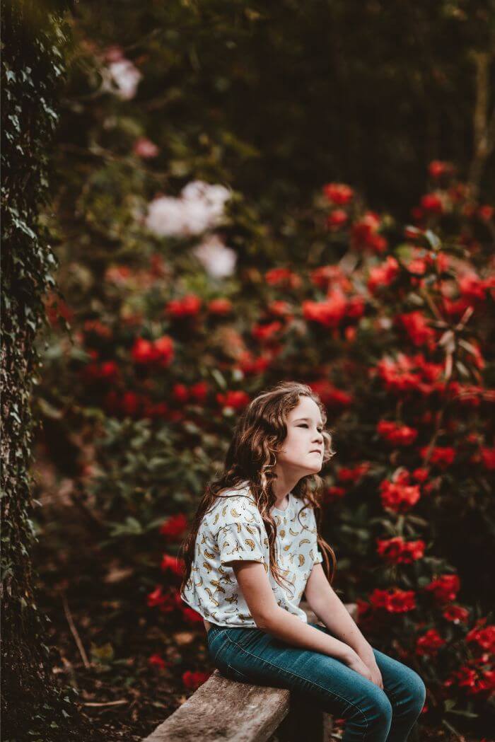 girl sitting on bench beside the red flowers