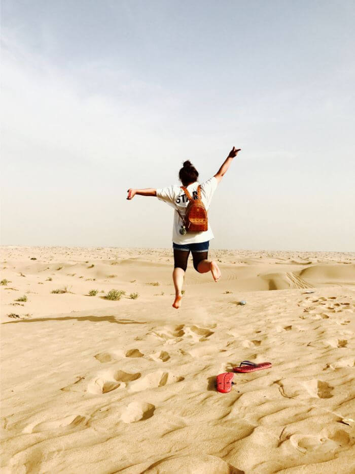 woman jumping on brown sand during daytime